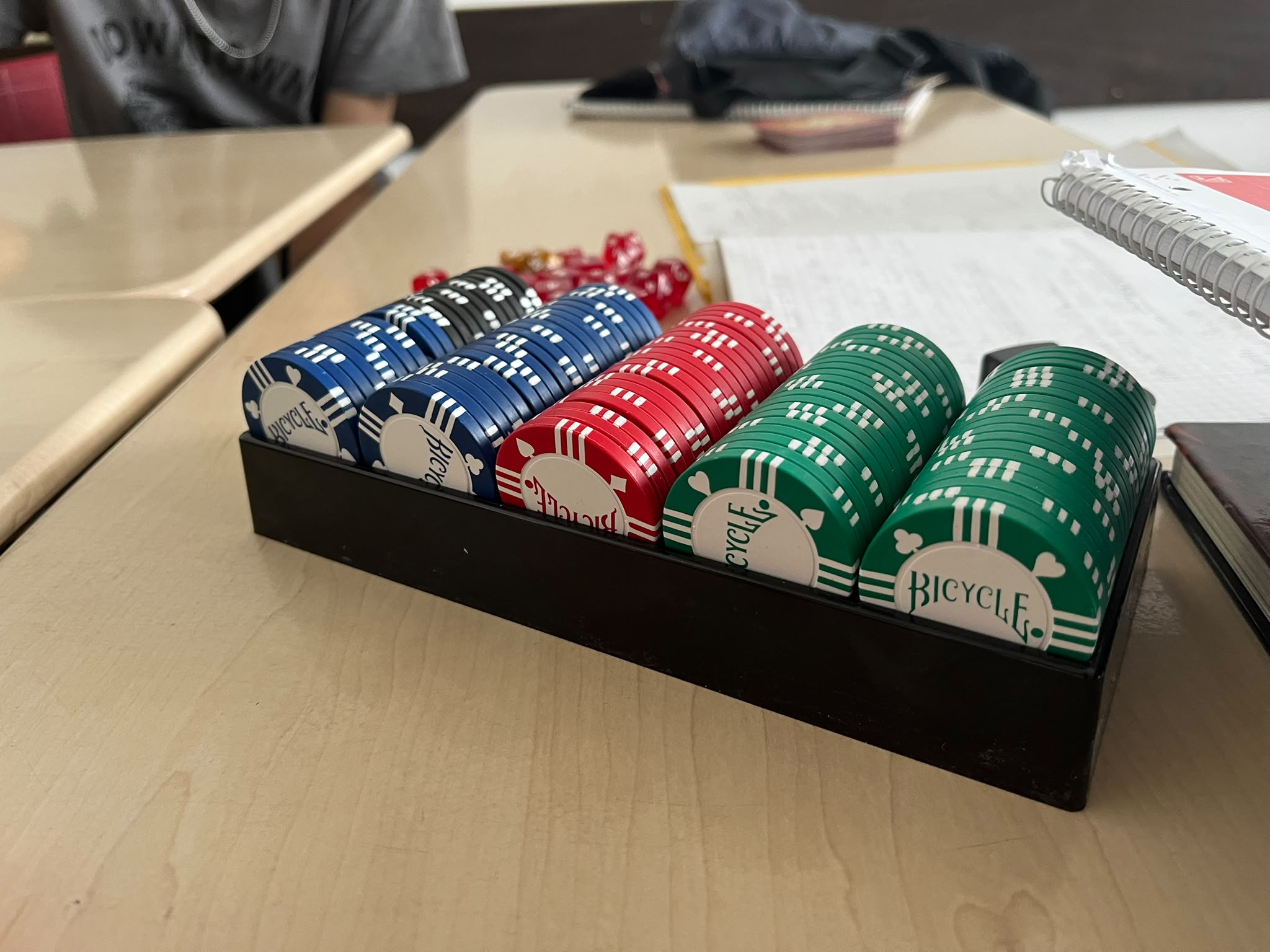 Pokerchips in Schwarz, Blau, Rot und Grün in einer Ablage, im Hintergrund liegen Würfel