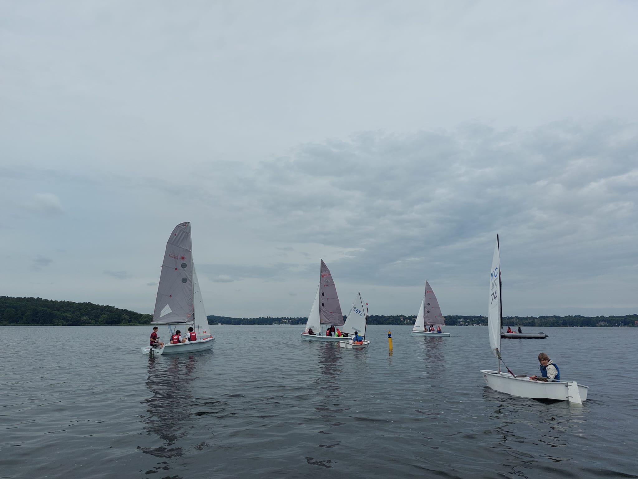Mehrere Segelboote mit Schülerinnen und Schülern auf dem Wannsee bei bewölktem Himmel